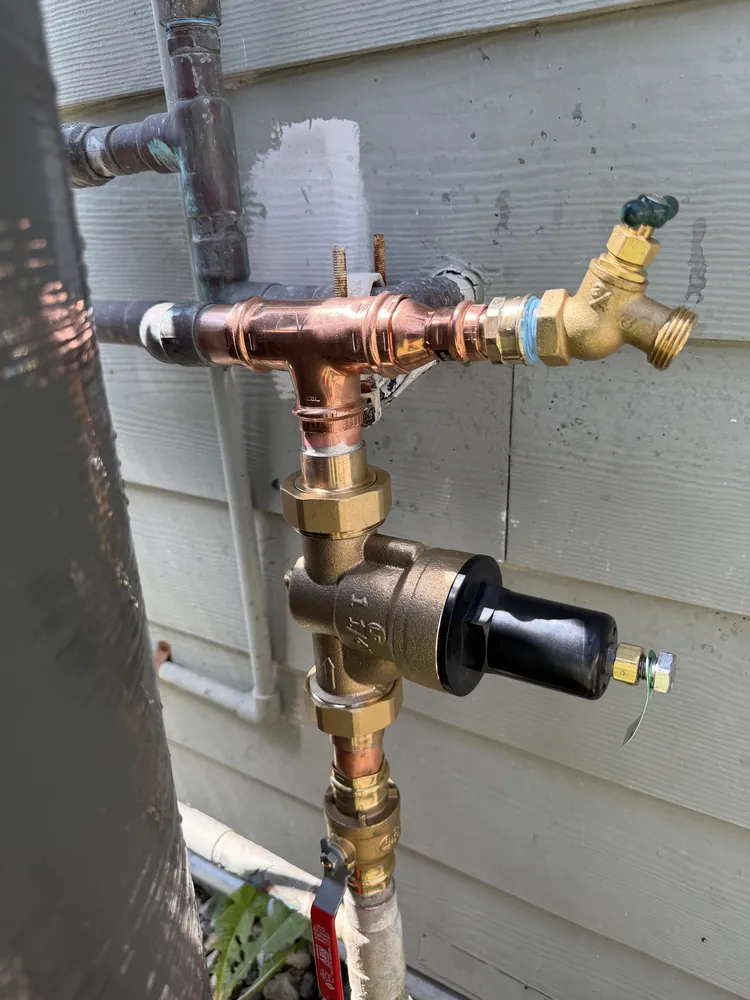 A new brass water pressure regulator and copper pipe fittings installed on an exterior wall